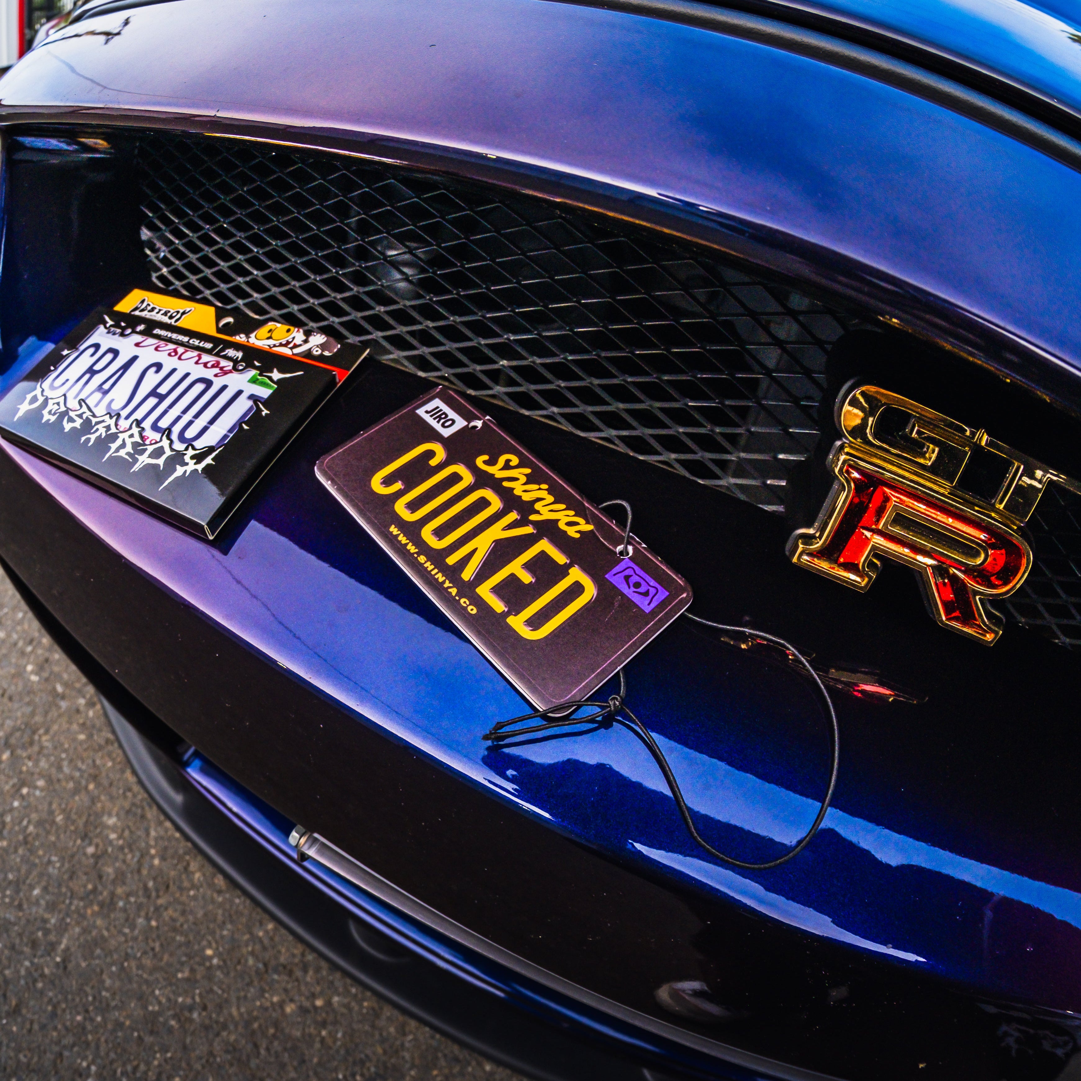 Close-up of a car's front grille with 'Cooked' license plate and 'GTR' badge.