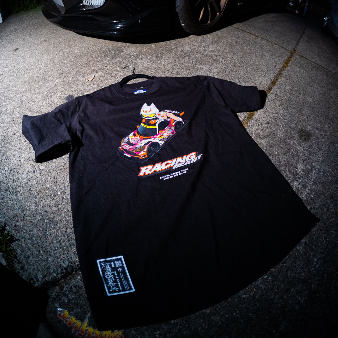 Black t-shirt with racing graphic on a concrete surface at night, with a car in the background.