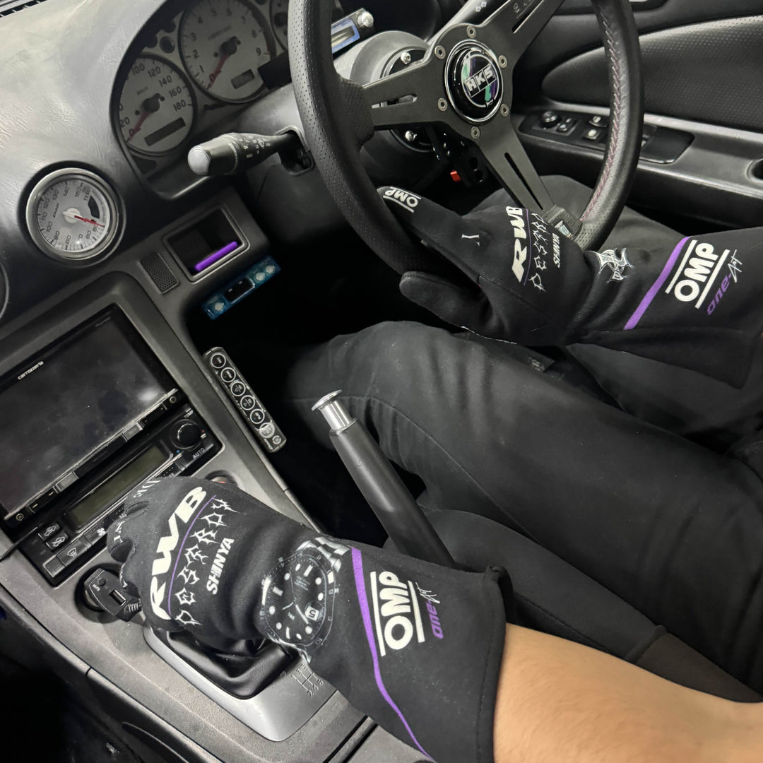 Person inside a car wearing gloves with 'OMP' branding.
