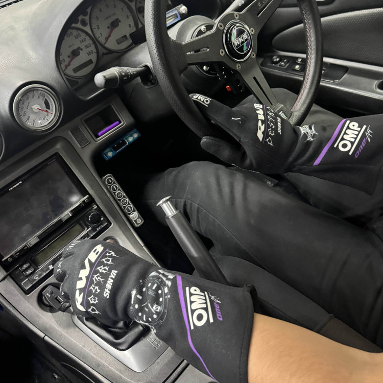Person inside a car wearing gloves with 'OMP' branding.
